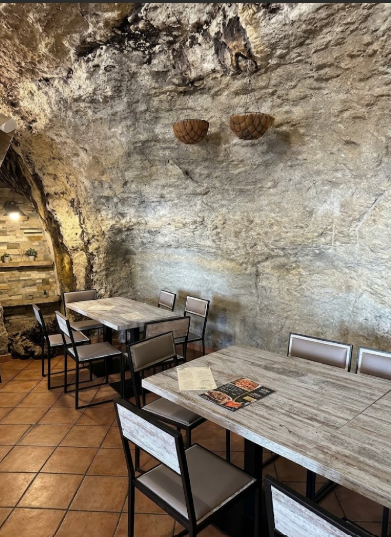 Comedor de Bar La Tasca con mesas de madera bajo la roca natural